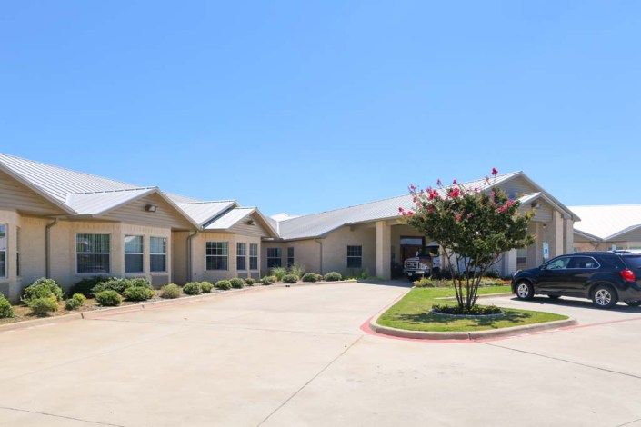 A single-story residential building with a driveway and landscaped surroundings under a clear blue sky.