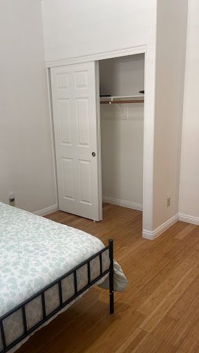 A simple and minimalist bedroom featuring a bed with light-colored bedding and an adjacent closet.