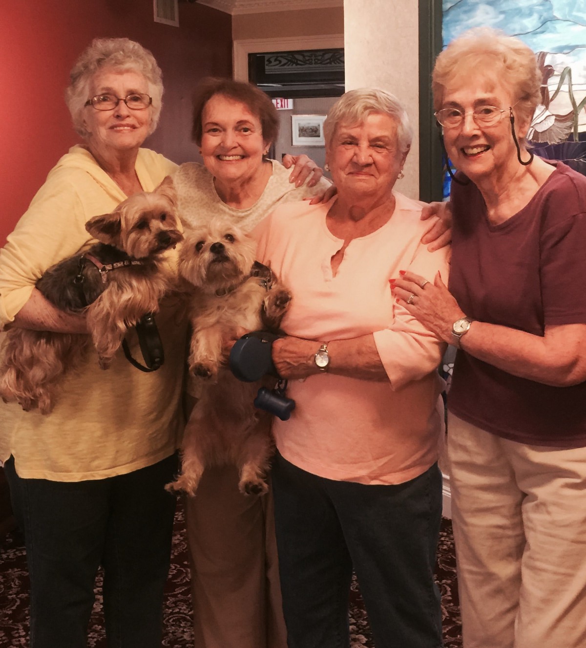 A group of women posing together indoors with two small dogs.