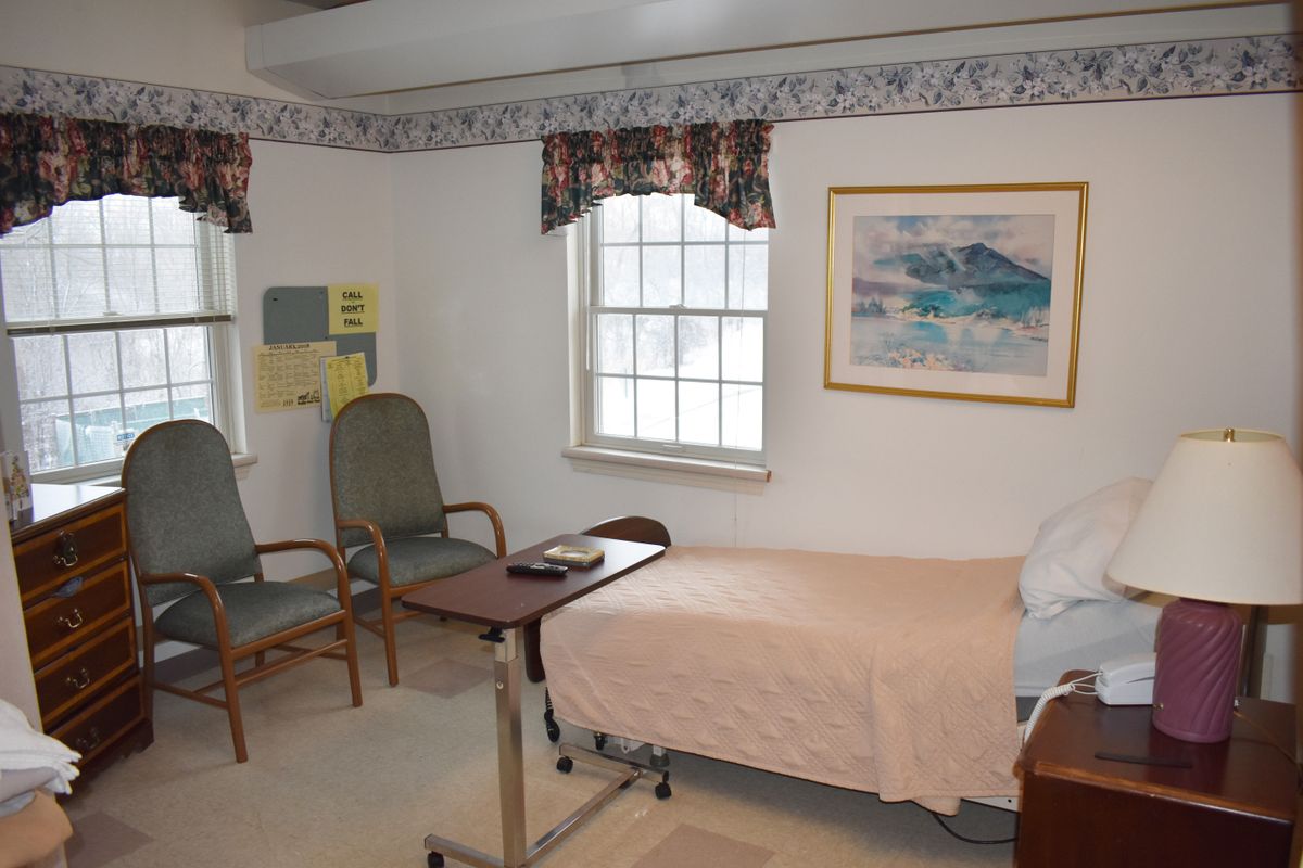 A hospital room with a patient bed, two chairs, and a window.