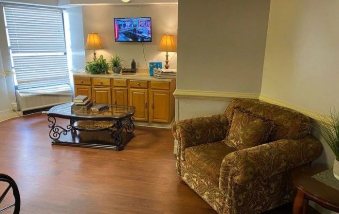 A cozy living room with a patterned armchair, glass coffee table, and wall-mounted television.