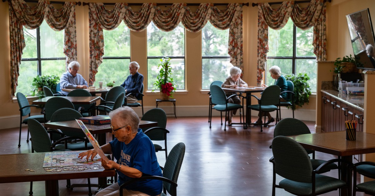 Elderly individuals relaxing and socializing in a community room setting.