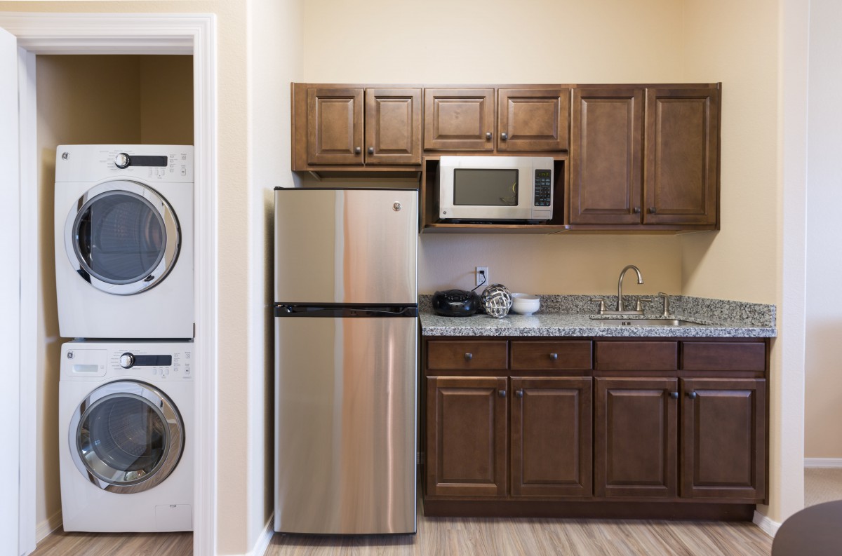 A modern kitchen with a stainless steel refrigerator and microwave, alongside a stacked washer and dryer.