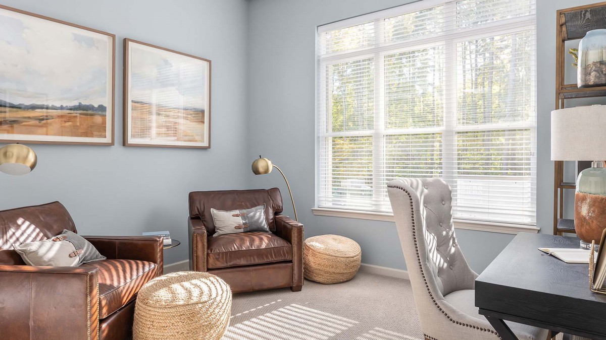 A cozy living room with a leather armchair, poufs, and natural light streaming through the window.