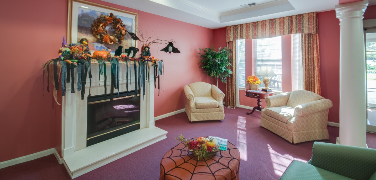 A cozy living room decorated for Halloween, featuring a fireplace adorned with seasonal decor, two comfortable armchairs, and a coffee table with a spiderweb cover.