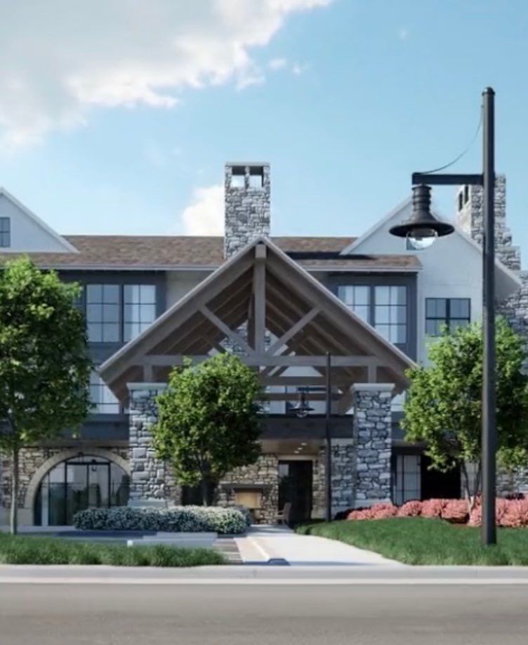 A modern building with a rustic design, featuring stone and wood elements, surrounded by trees and landscaping.