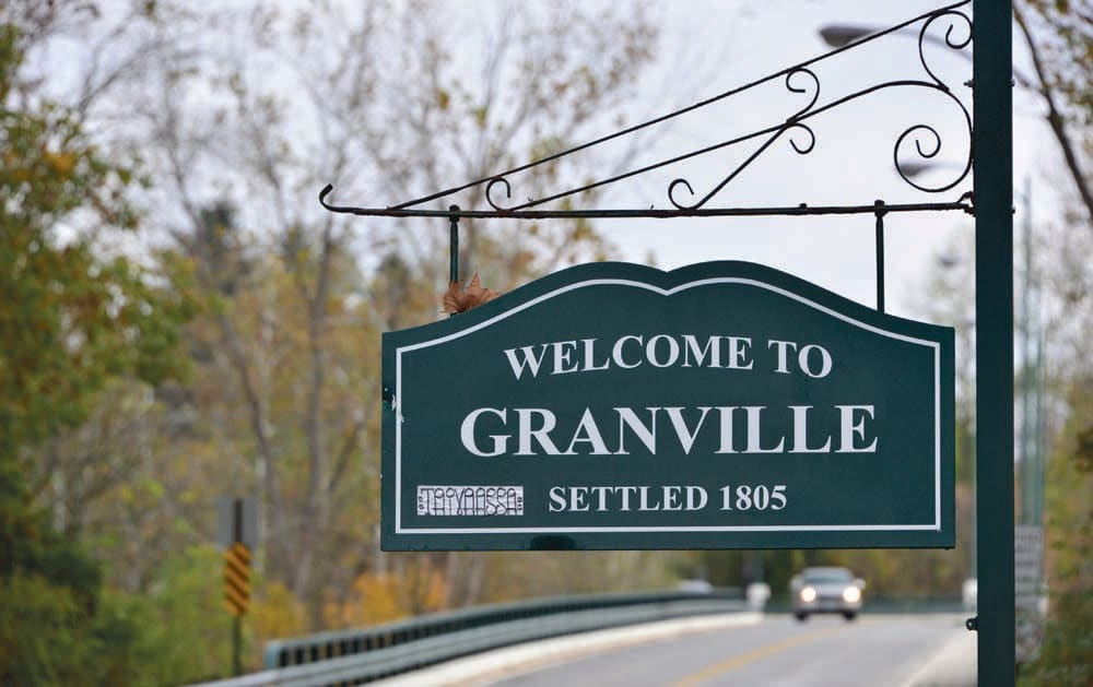 A welcome sign for the town of Granville, established in 1805, located by a road surrounded by trees.