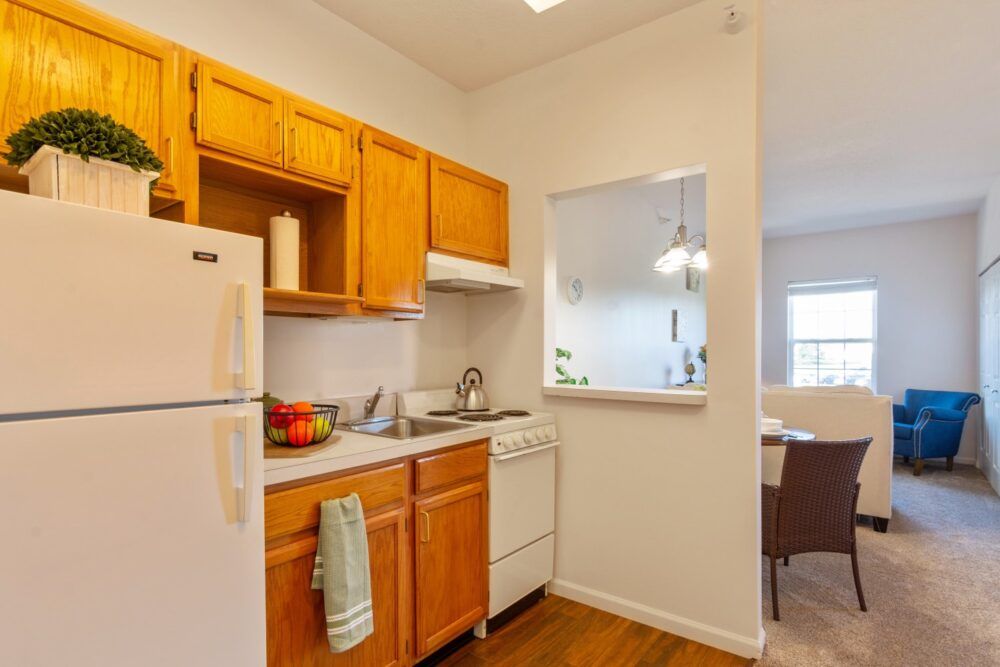 A cozy apartment kitchen with wooden cabinets, a refrigerator, stove, and sink.