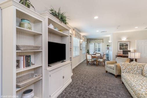 A cozy living room with a television and shelving unit, leading to a dining area.