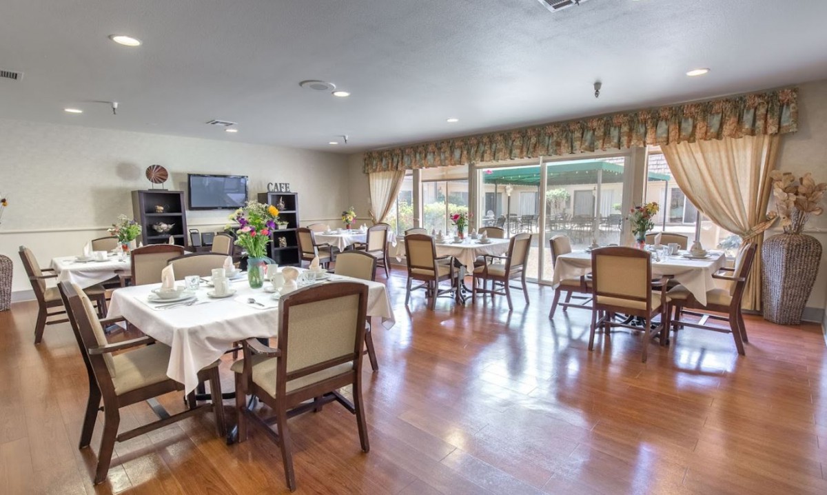 A spacious dining area with neatly arranged tables and chairs, featuring large windows and hardwood flooring.