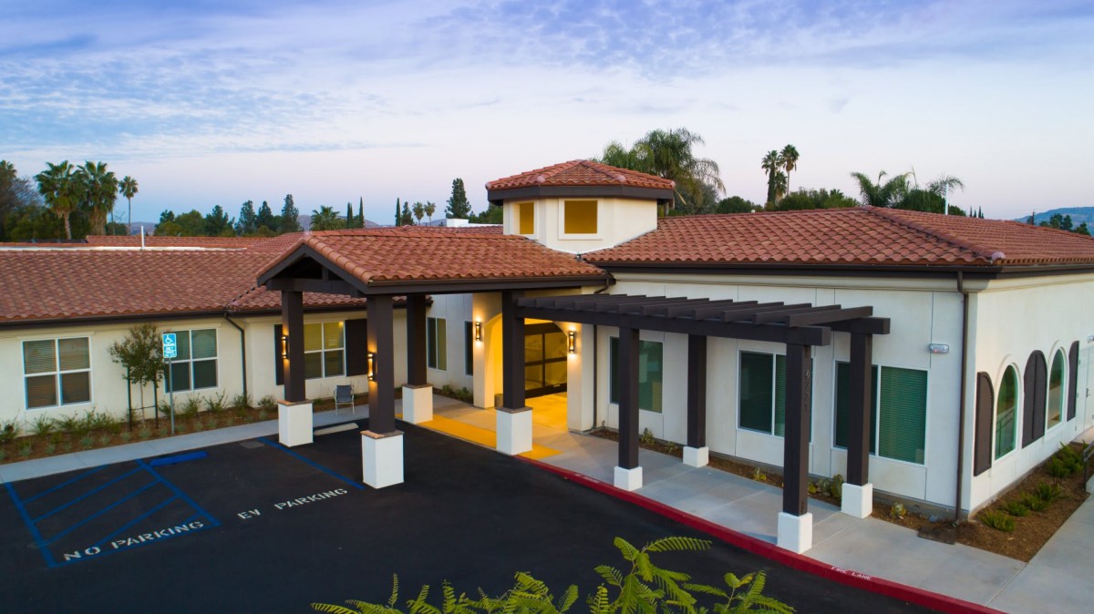 A modern building with a covered entrance and spacious driveway, featuring a tiled roof and well-maintained exterior.
