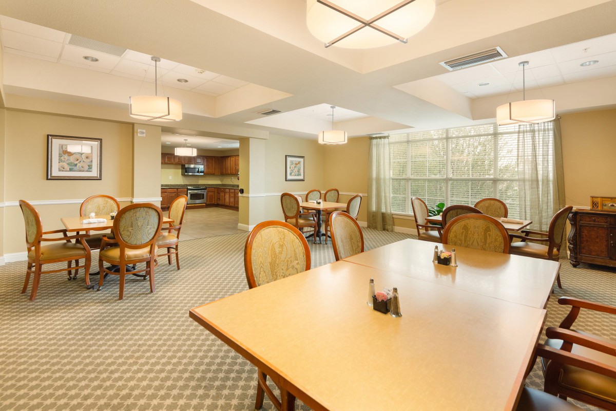A well-lit dining room with multiple tables and chairs, featuring elegant lighting fixtures and large windows.