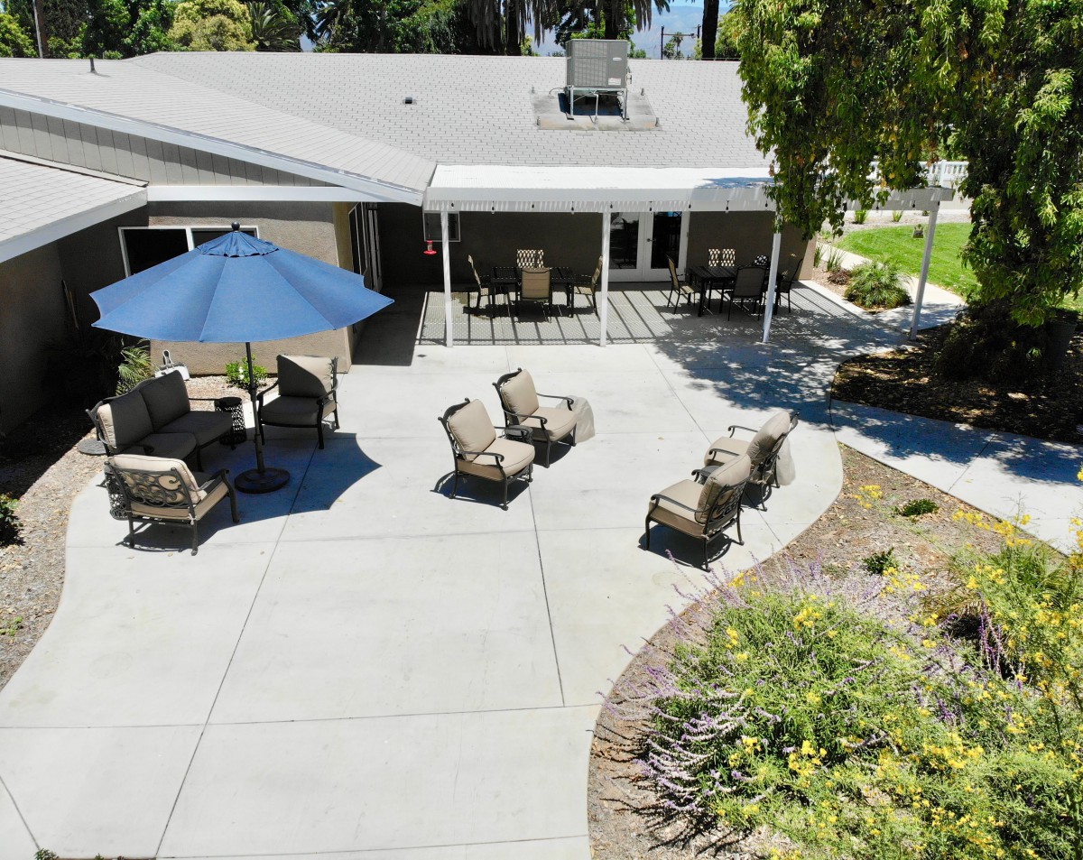 A well-furnished backyard patio with seating and an umbrella, surrounded by a landscaped garden.