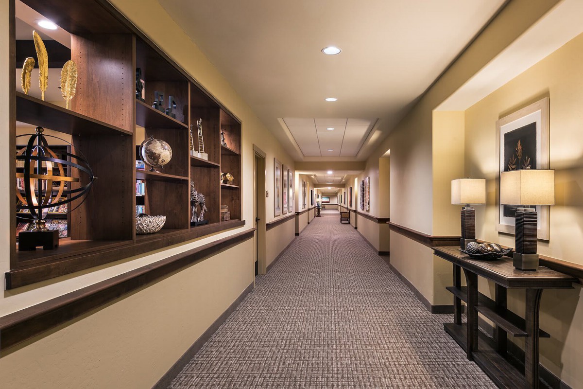 A well-lit hotel hallway with decorative shelving and carpeted flooring.