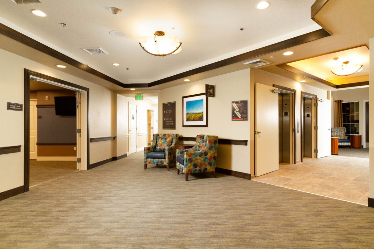 A modern hallway featuring elevators, comfortable seating, and decorative wall art.