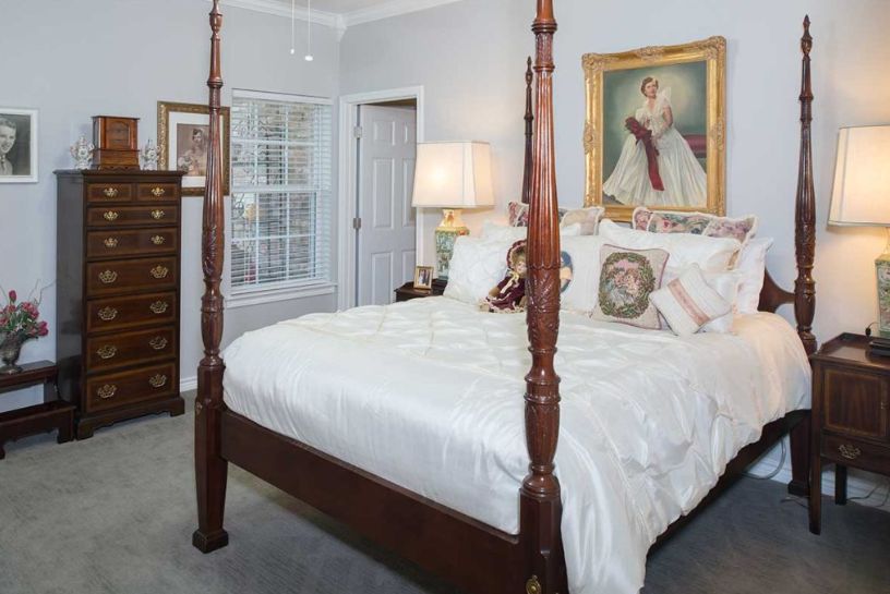 A cozy bedroom featuring a traditional four-poster bed, decorative pillows, and an elegant painting on the wall.