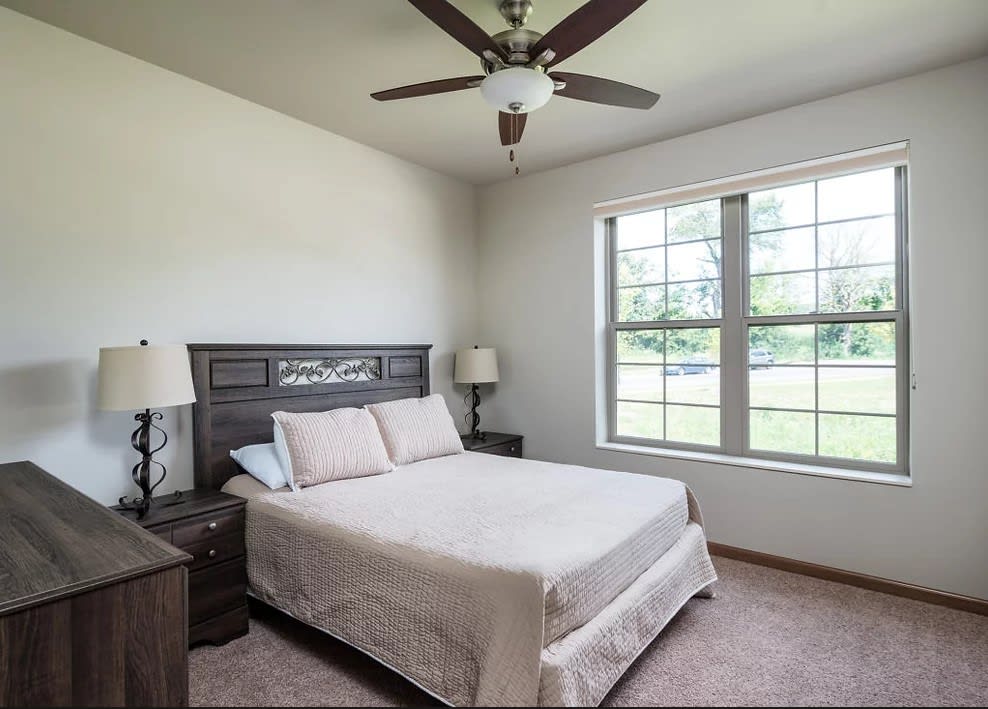 A minimalist bedroom with a bed, ceiling fan, and large window.
