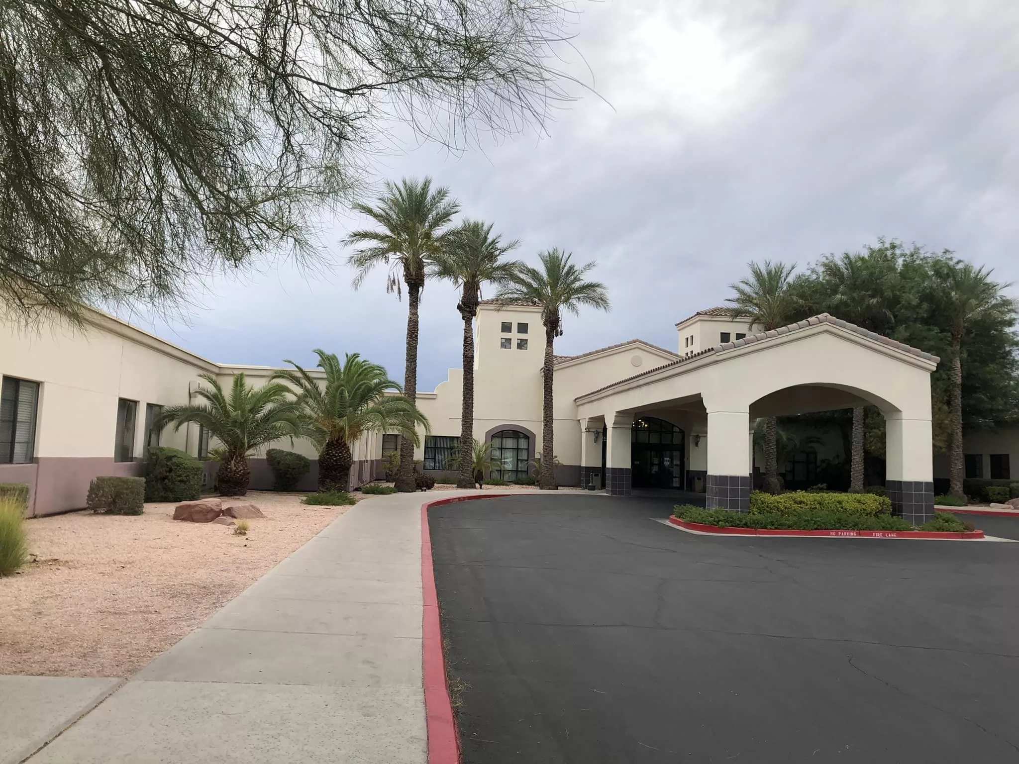 A building with palm trees and a driveway leading to the entrance.