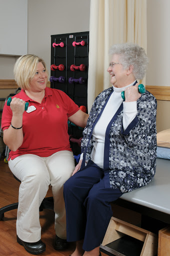 A healthcare professional guides a senior woman in an exercise session using dumbbells for strength training.