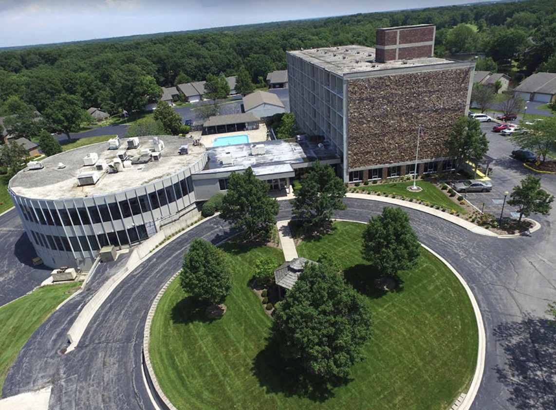 An aerial view of a building surrounded by landscaped greenery and roads.