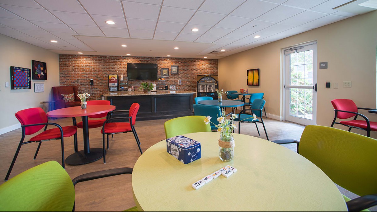 A modern lounge with colorful seating, tables, a television, and a coffee station.