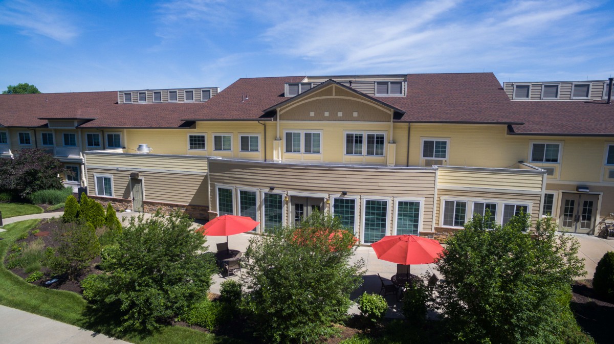 A view of a hotel with a landscaped garden and red umbrellas on the patio under a blue sky.