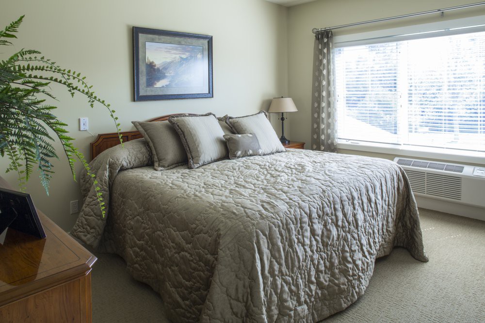 A cozy bedroom with a neatly made bed, framed artwork on the wall, and natural light coming through the window.