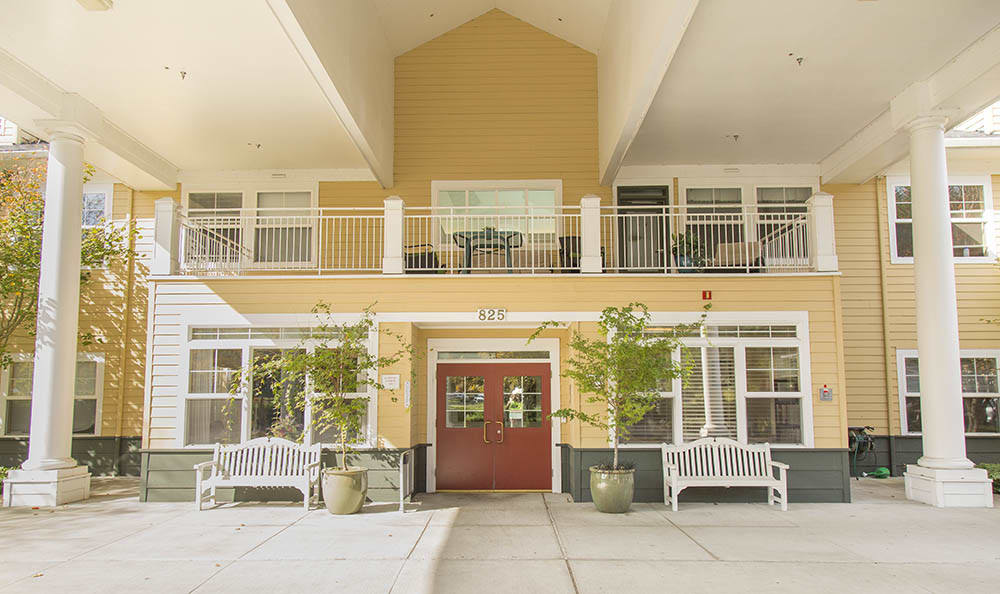 A two-story building entrance with a red door, benches, and potted plants.