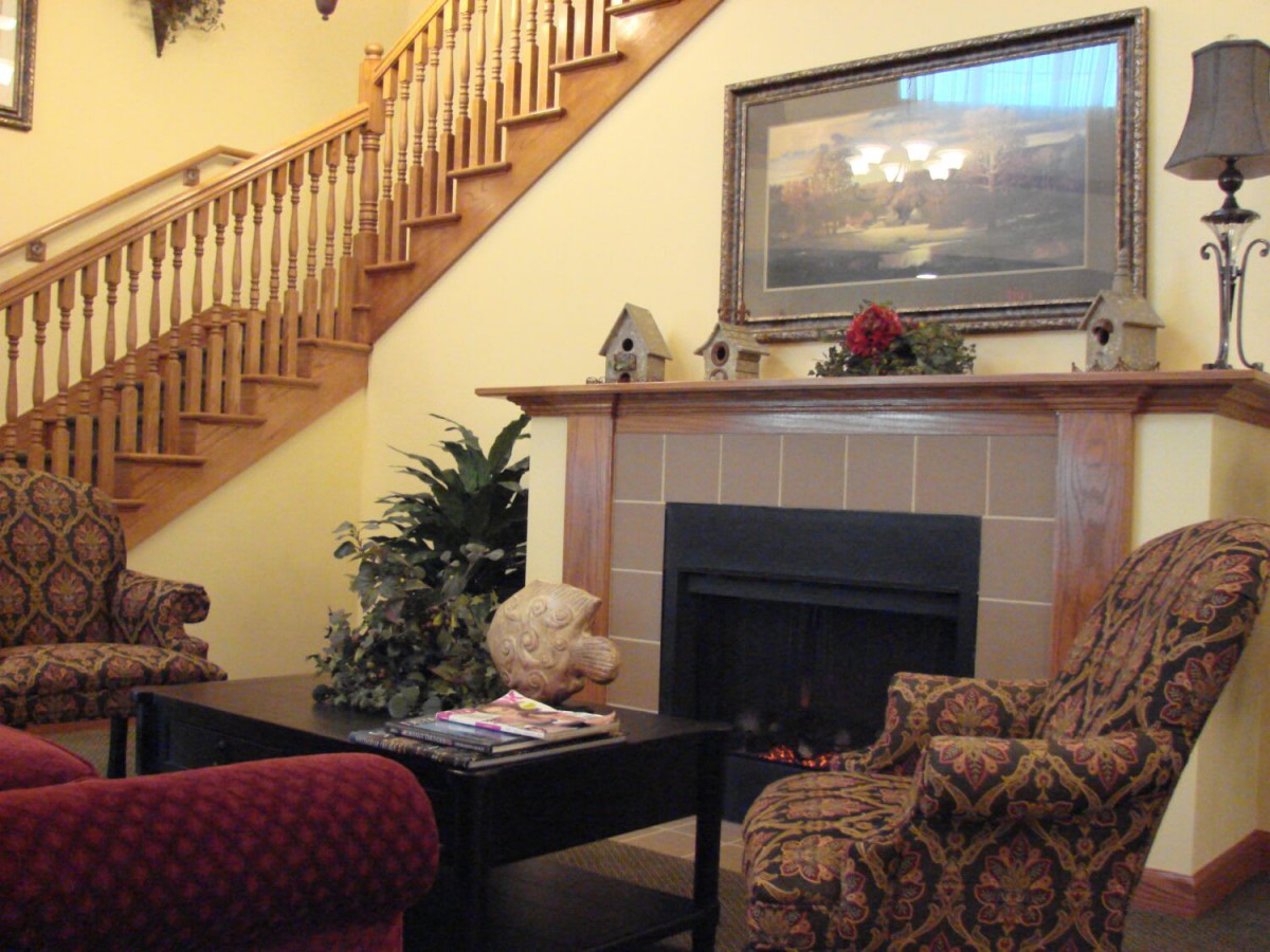 A cozy living room featuring a fireplace, patterned chairs, and a wooden staircase.