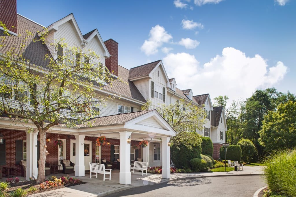 A charming residential building with a porch and trees under a blue sky.