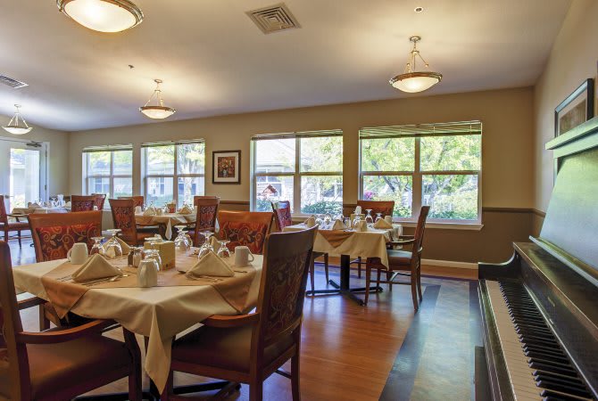 A well-lit dining room with neatly arranged tables and chairs, featuring large windows and elegant lighting.