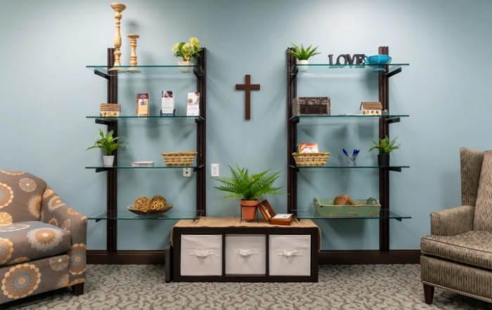 A well-organized and decorated room with shelves featuring plants, decor items, and a cross on the wall.