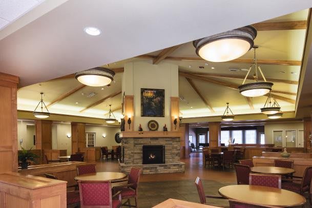 A cozy dining area with wooden furniture and a central fireplace, illuminated by ceiling lights.