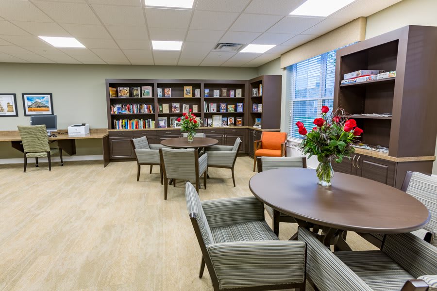 A cozy library space with bookshelves, tables, and chairs, adorned with flower arrangements.