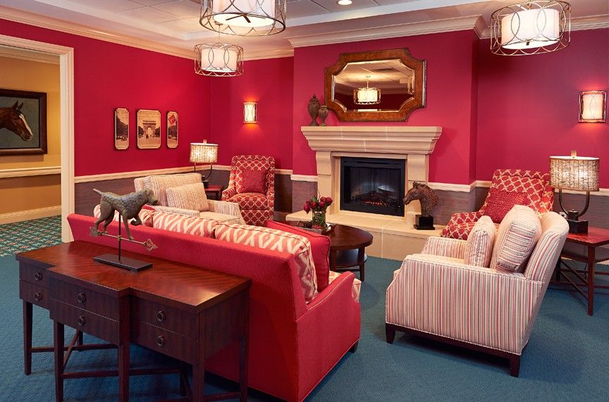 A warmly decorated living room with red walls, elegant furniture, and a central fireplace.