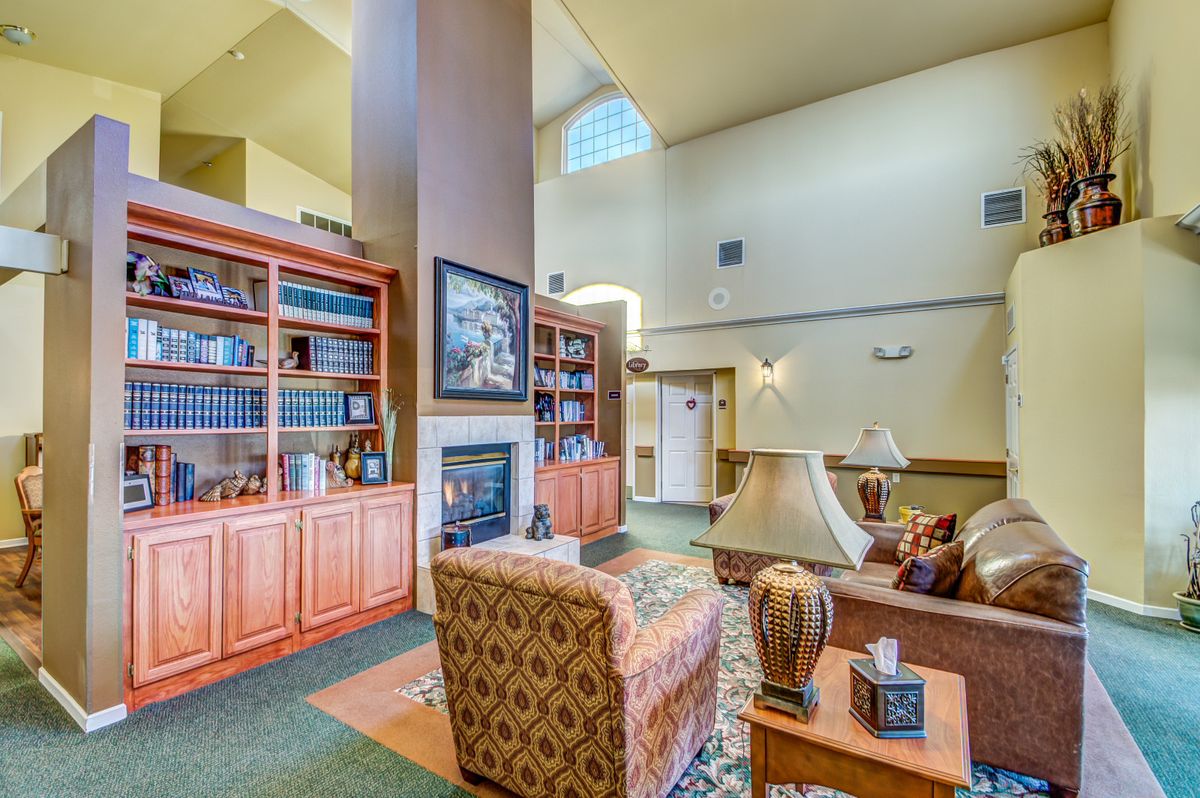 A cozy living room with tall bookshelves and a fireplace, featuring comfortable furniture and high ceilings.