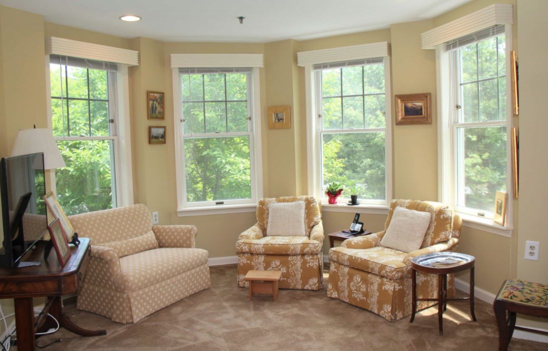 A cozy living room with armchairs and a sofa by large windows, creating a bright and inviting atmosphere.