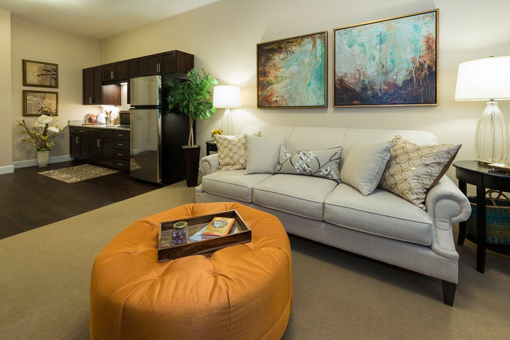A modern living room with a comfortable sofa, vibrant artwork, and an orange ottoman.