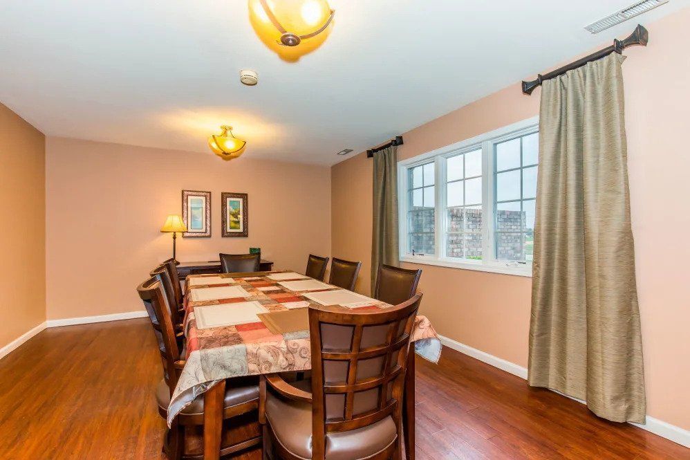 A spacious dining room with a large table and chairs, featuring warm lighting and window curtains.