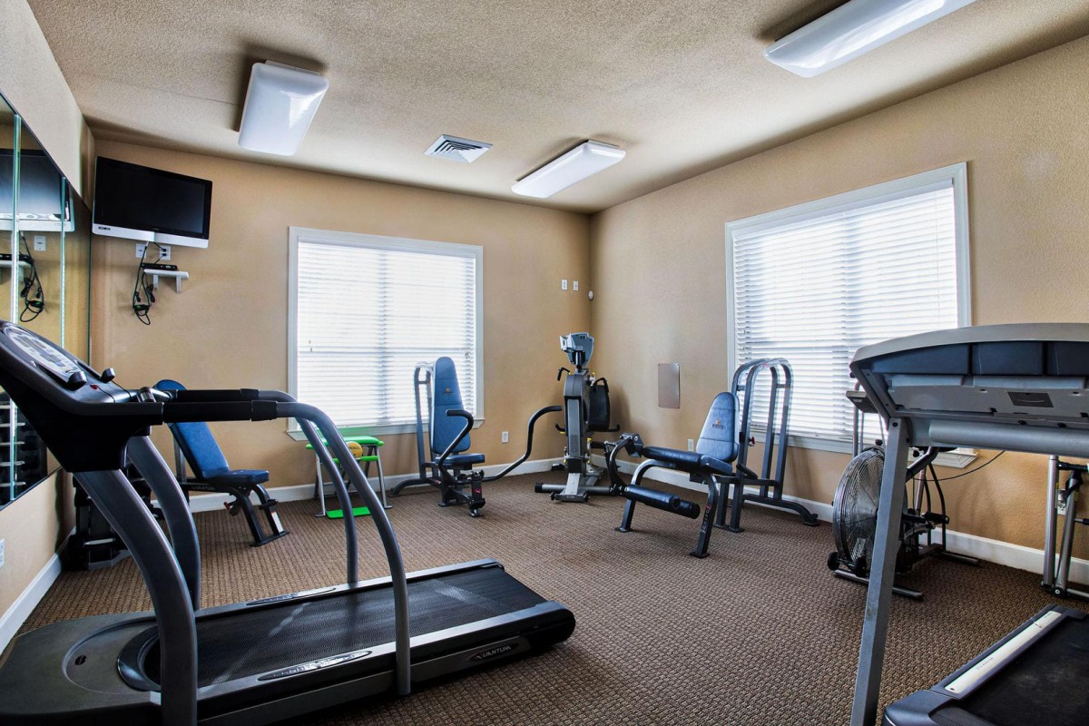 A brightly lit gym with various exercise equipment including treadmills and stationary bikes.