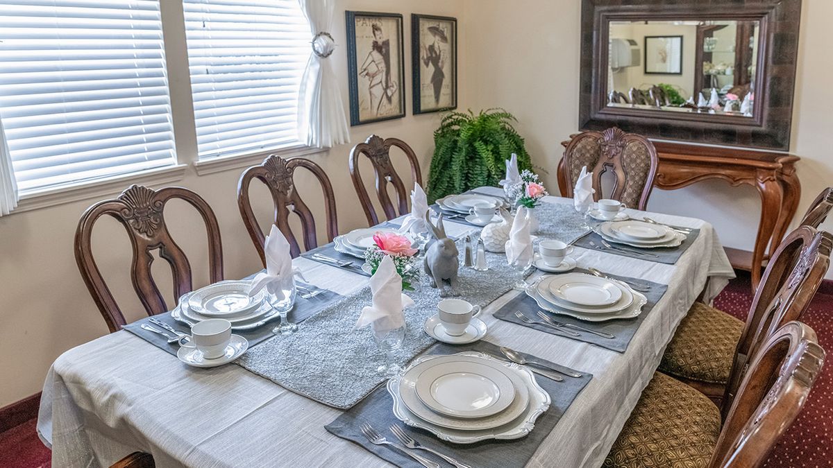 An elegantly set dining table with plates, cutlery, and decorations in a well-lit room adorned with artwork.