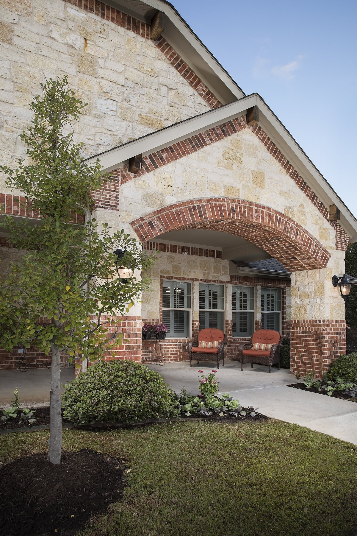 A cozy porch with brick and stone accents, featuring outdoor seating and surrounding greenery.