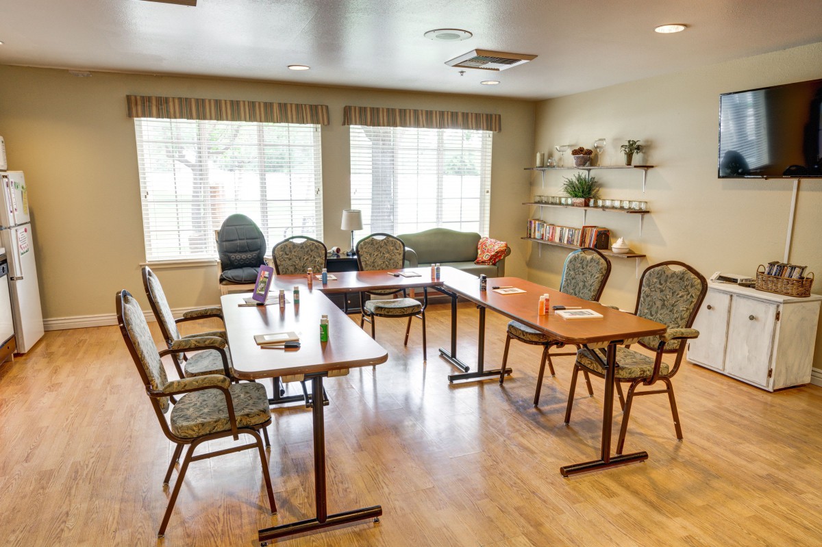 A well-lit meeting room with arranged tables and chairs, featuring large windows.