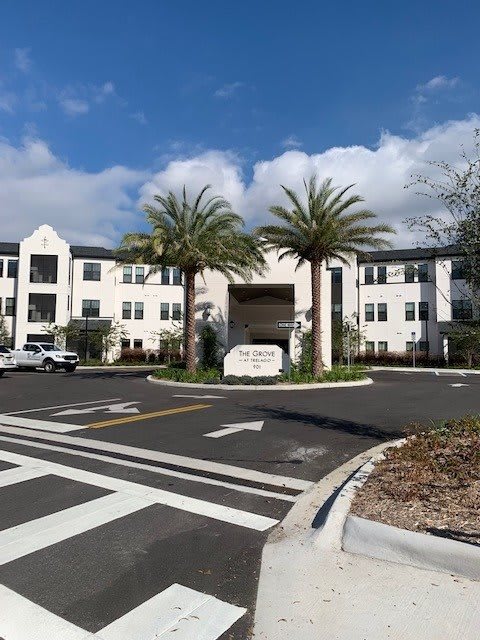 A modern building with palm trees at the entrance under a partly cloudy sky.