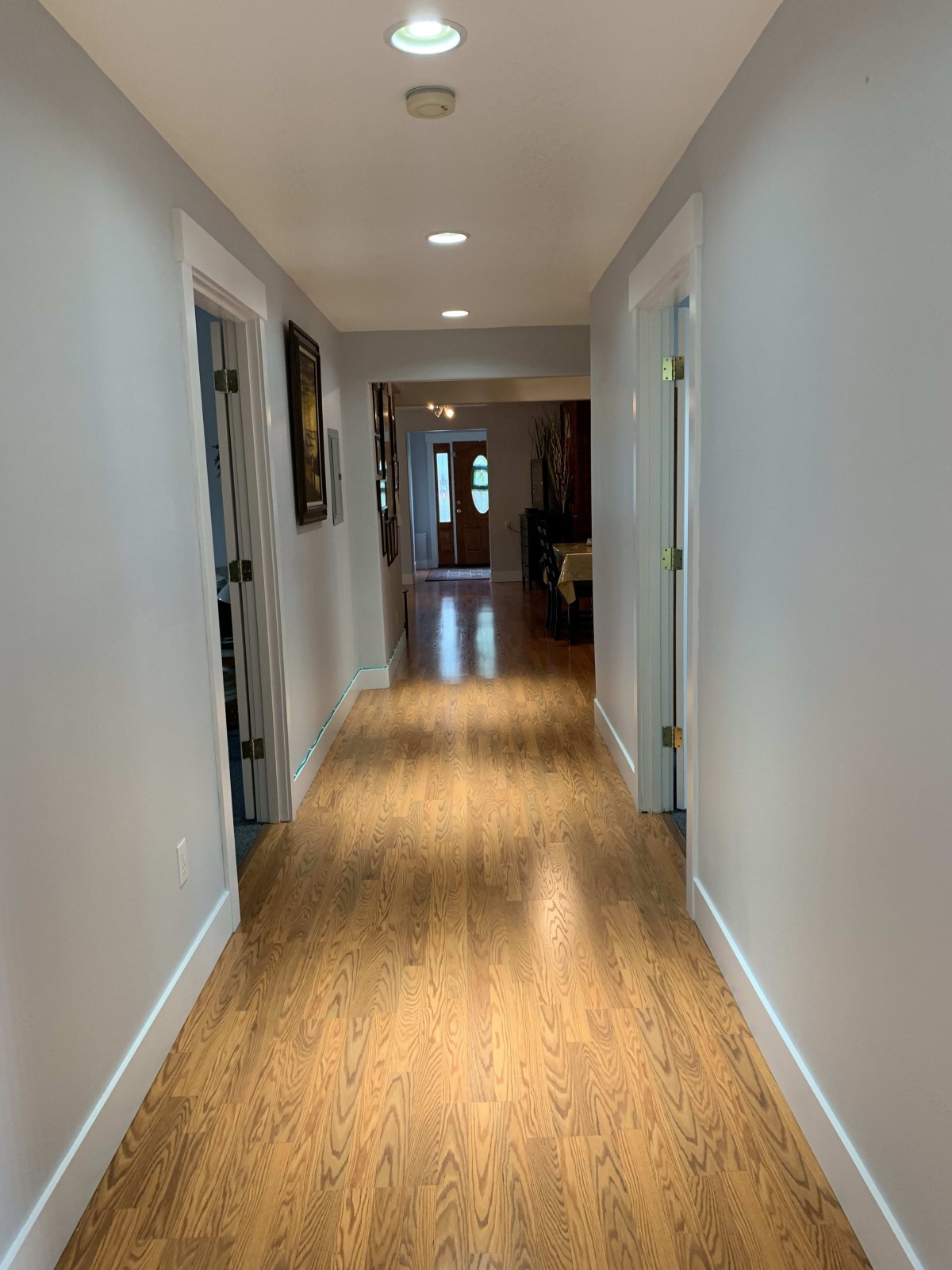A well-lit hallway with wooden flooring and multiple doors.