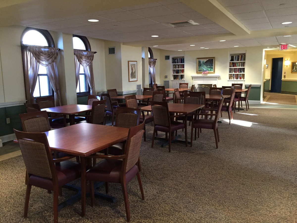 A spacious dining area with multiple tables and chairs, well-lit by natural light from the windows.