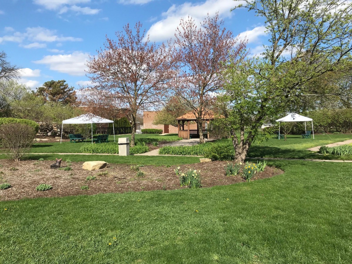 A peaceful park scene with gazebos, trees, and lush green grass under a partly cloudy sky.