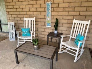 A cozy patio area with white rocking chairs and a coffee table, adorned with plants and turquoise pillows.