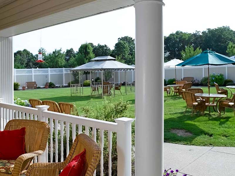 An inviting outdoor patio with wicker chairs overlooking a garden with gazebos and a white fence.