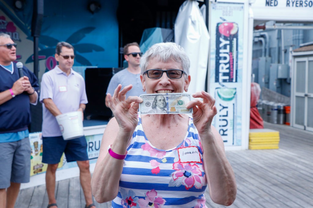 A woman smiling and holding up a dollar bill at an outdoor event.